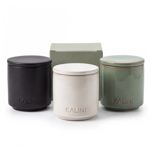 Black, ivory and green round ceramic candle jars beside a box